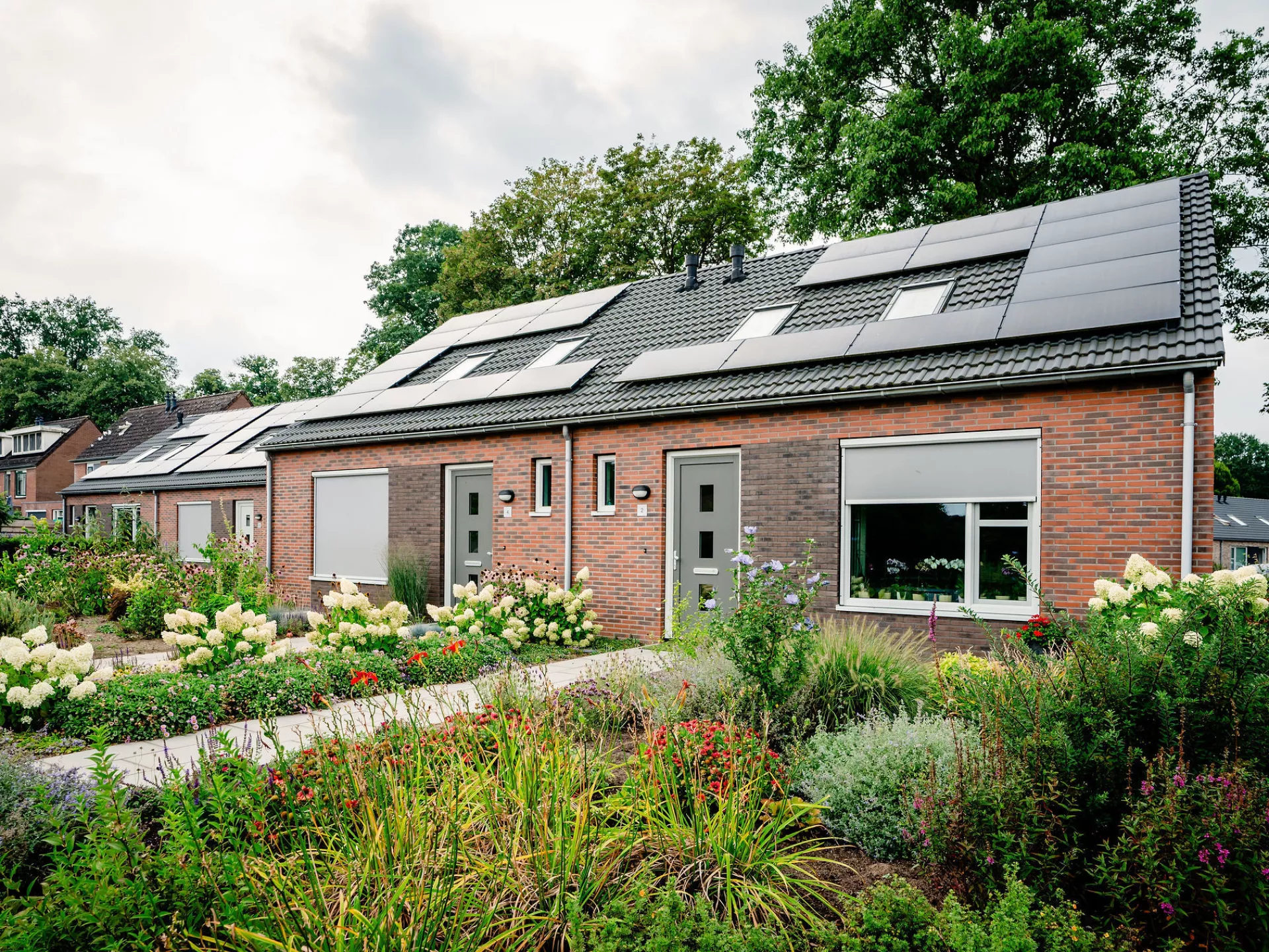 Een blok van twee woningen met zonnepanelen en een goed onderhouden tuin ervoor