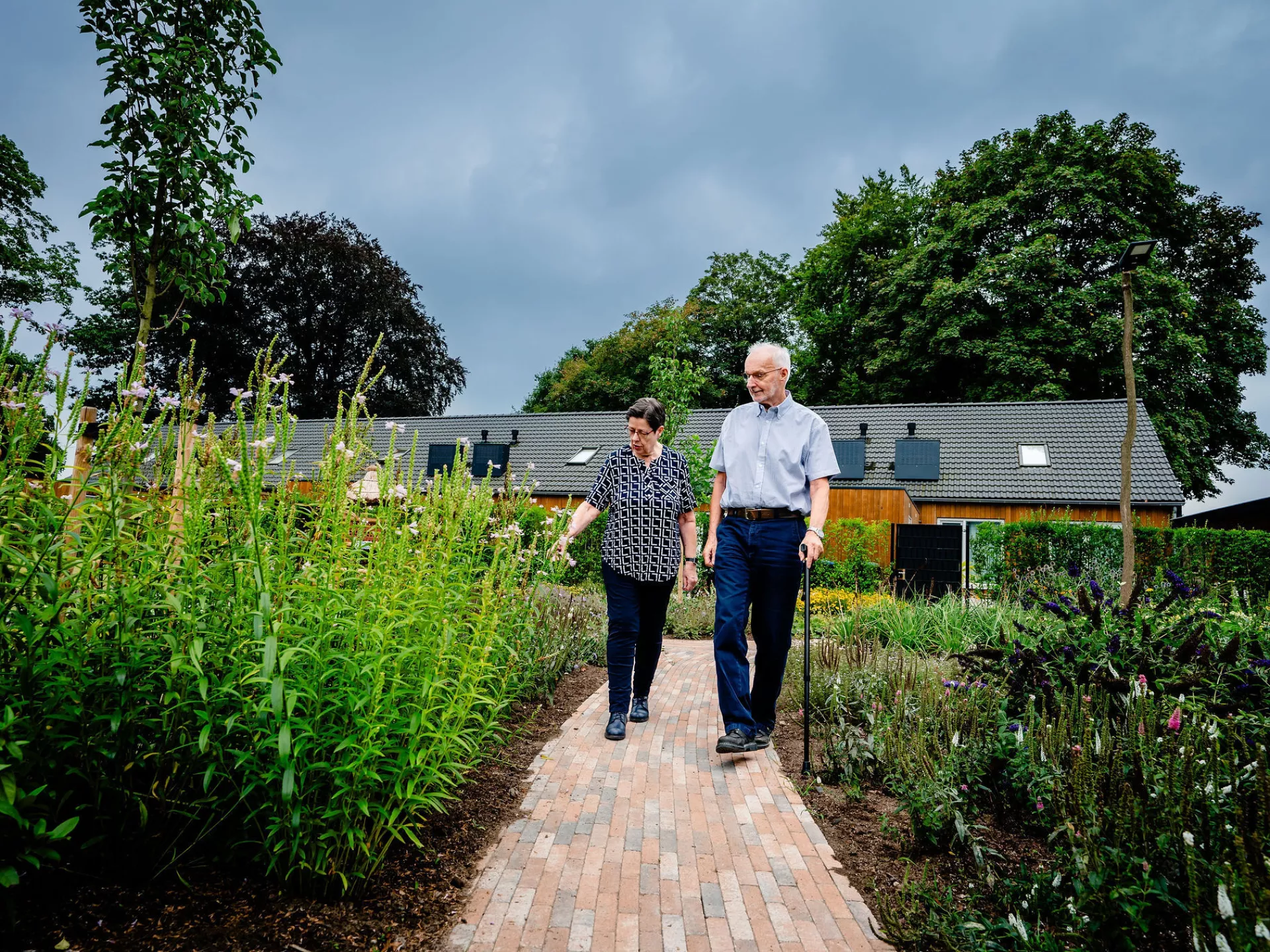 Een ouder echtpaar loopt naast elkaar over een stenen pad door een tuin