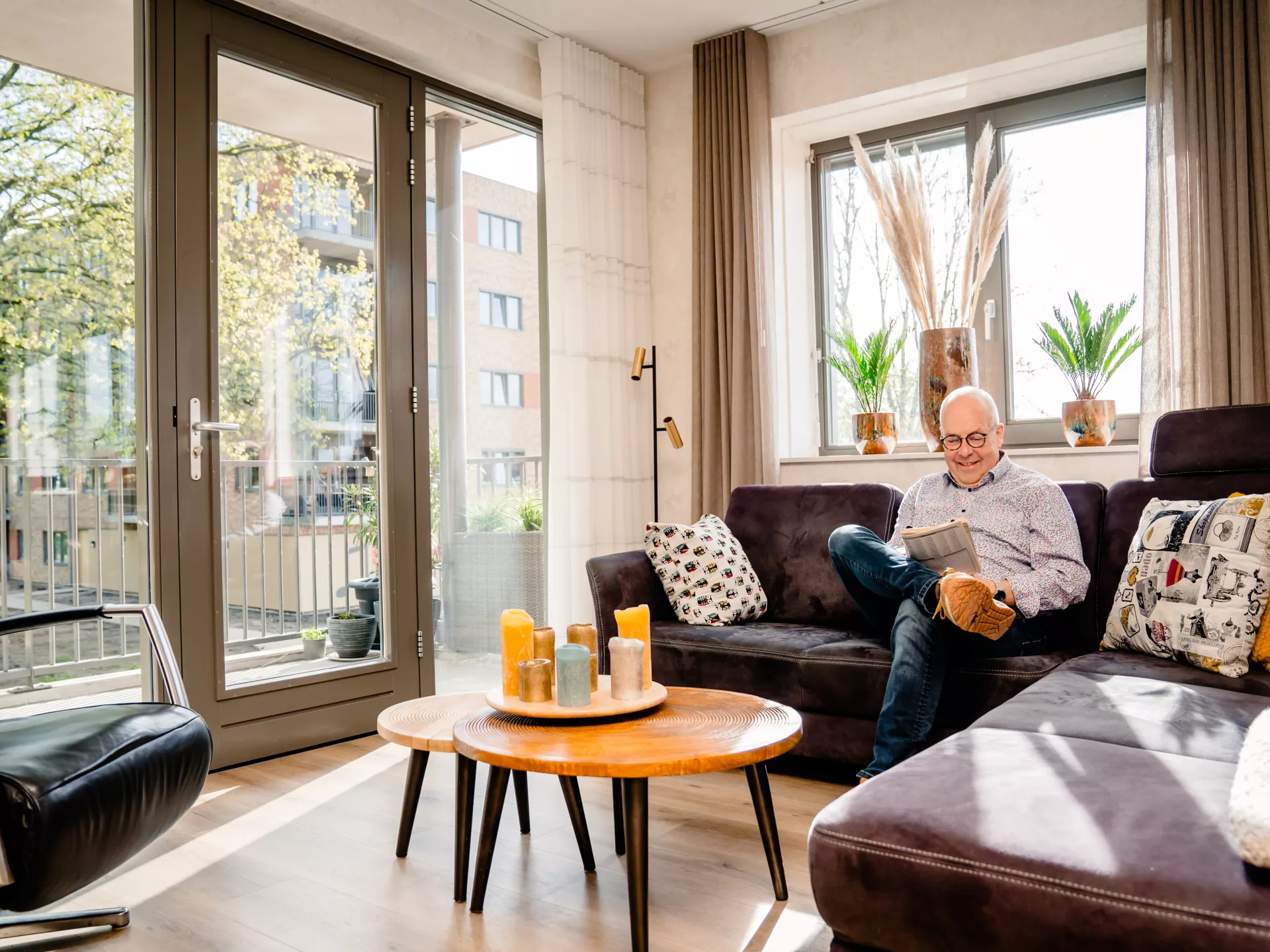 Een oudere man zit op de bank in zijn woonkamer en leest een boekje