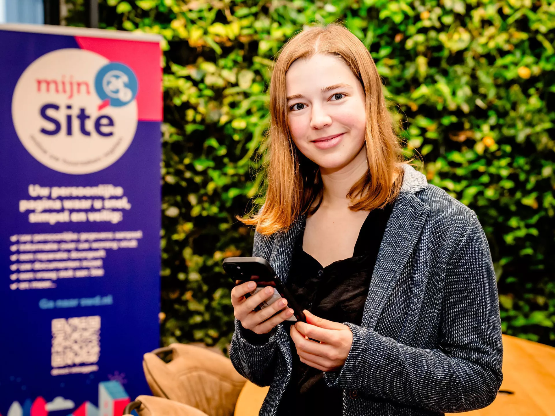 Dame met een mobiele telefoon in haar hand staat voor een groene kantoorwand