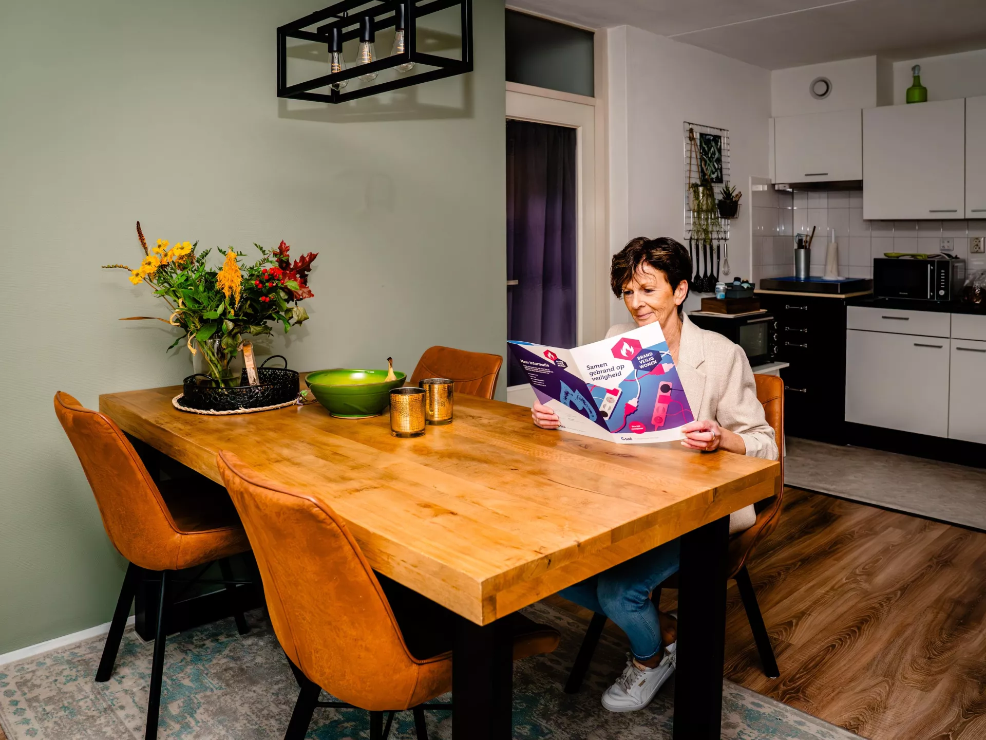 Een mevrouw leest een folder aan een houten tafel in haar keuken
