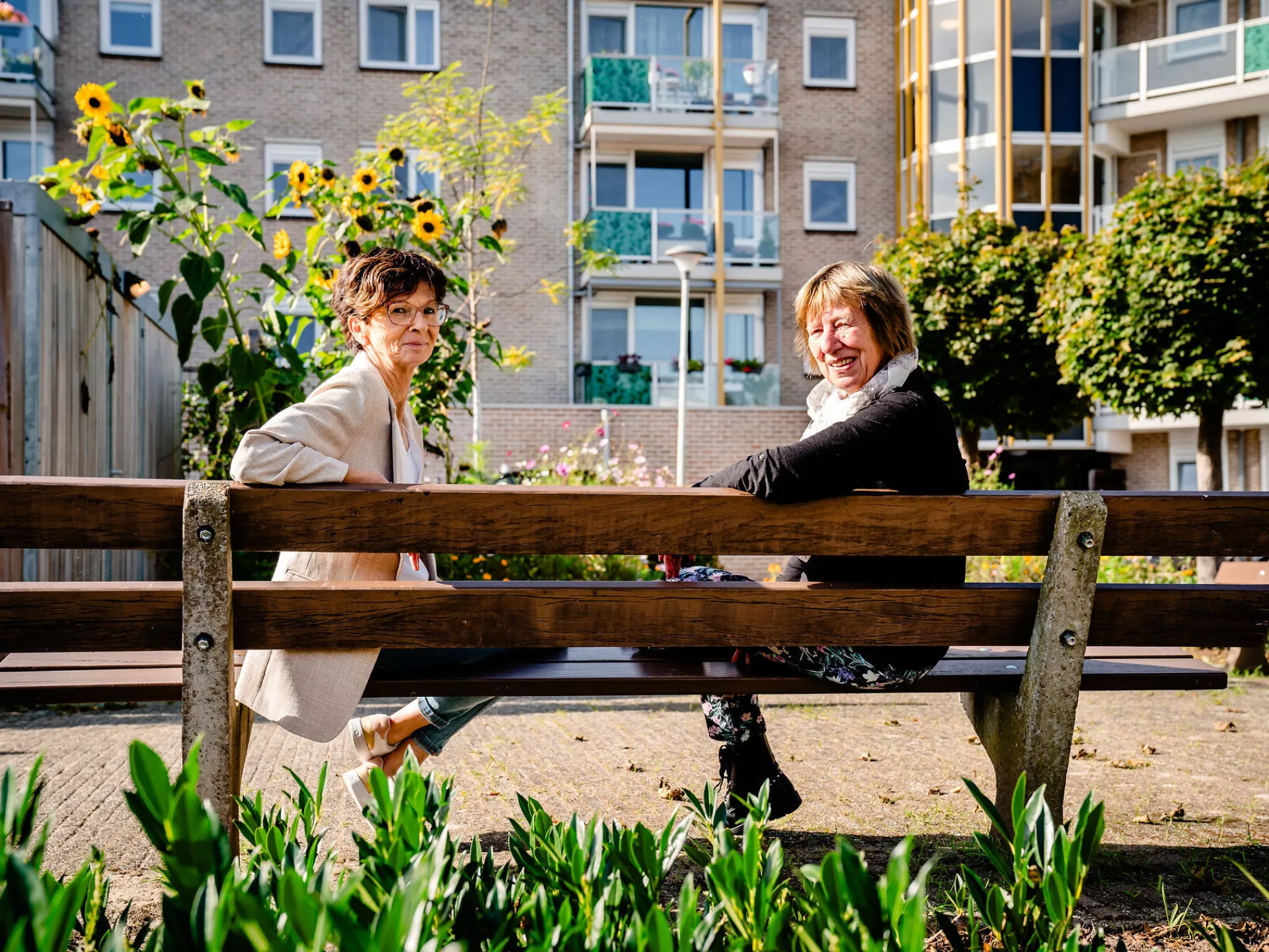 Twee dames zitten op een bank voor een appartementengebouw