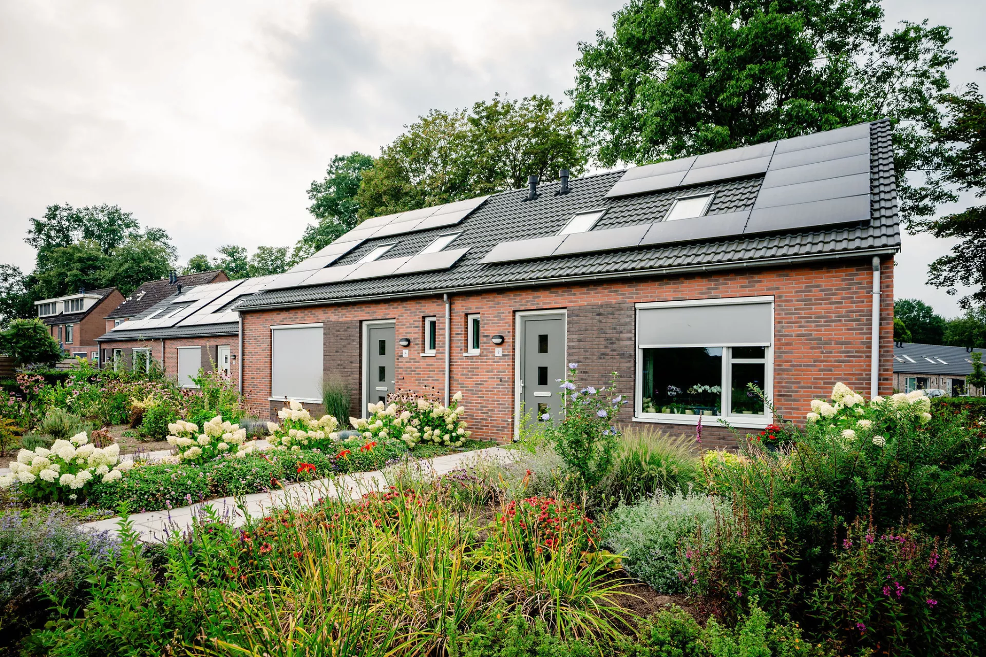 Een blok van twee woningen met zonnepanelen en een goed onderhouden tuin ervoor