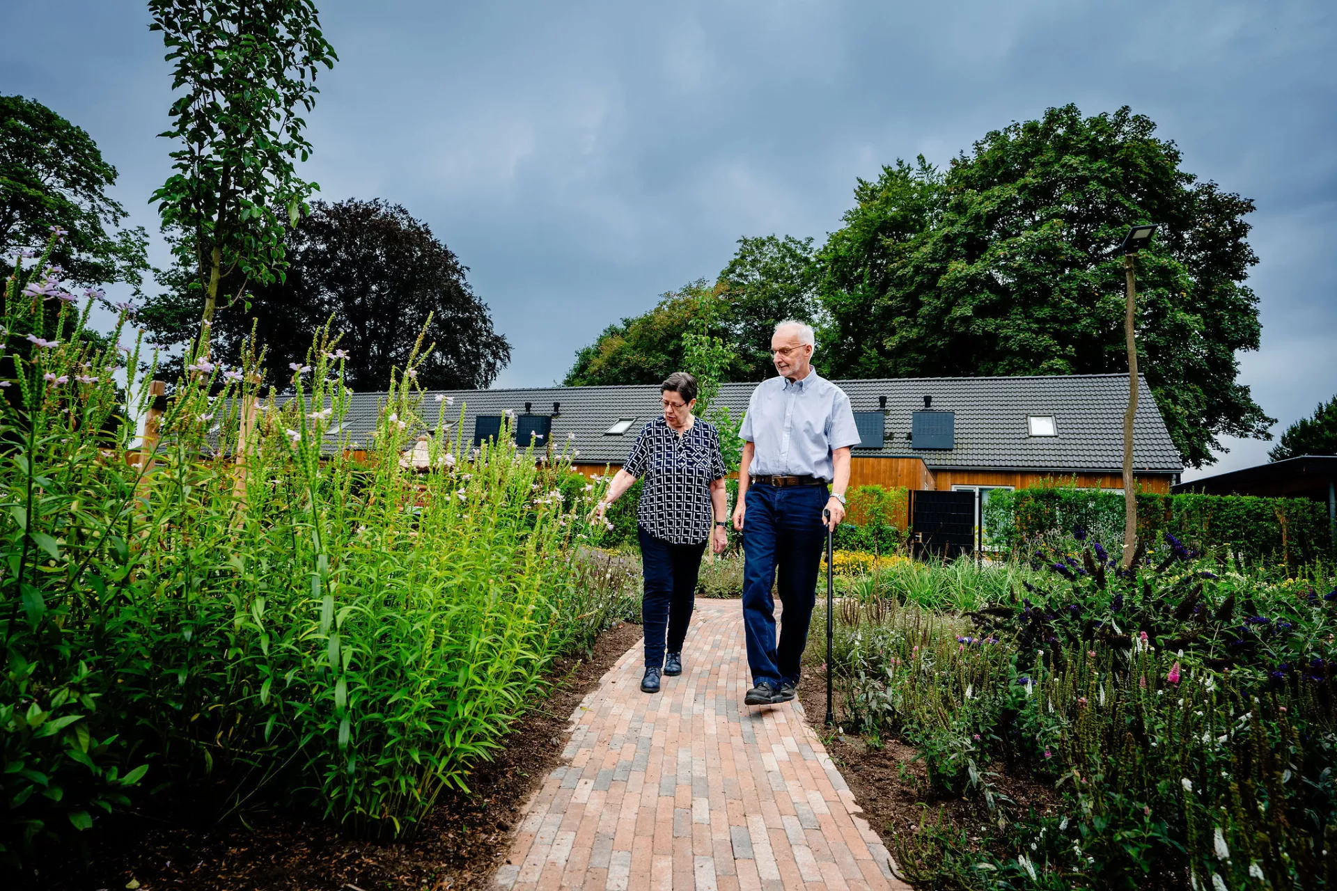 Een ouder echtpaar loopt naast elkaar over een stenen pad door een tuin