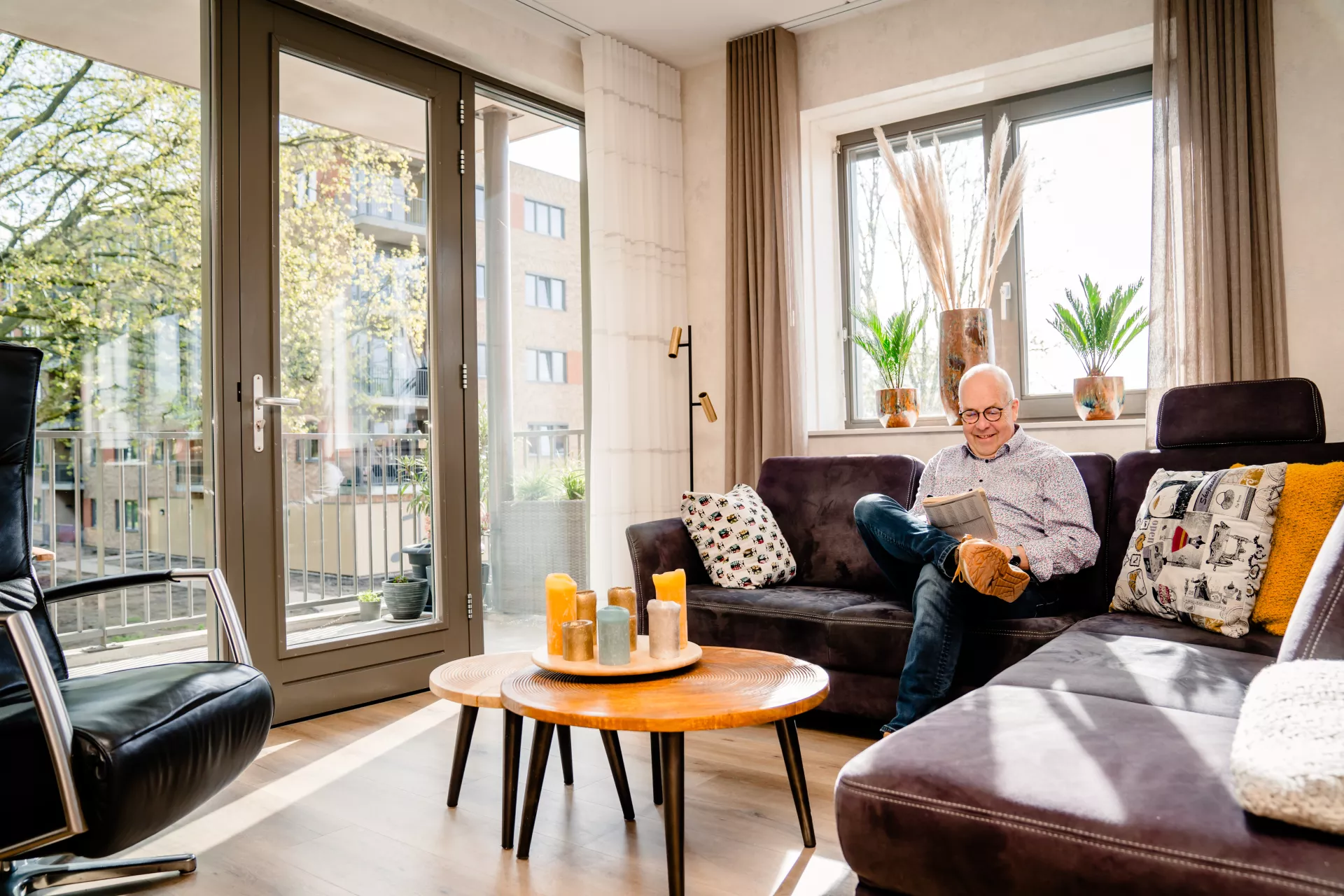 Een oudere man zit op de bank in zijn woonkamer en leest een boekje