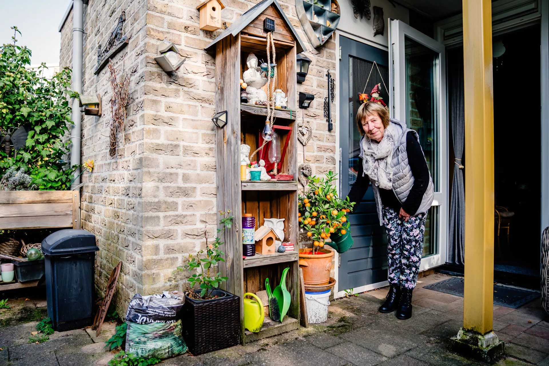 Een oudere dame geeft met een gieter een potplant in haar achtertuin water 