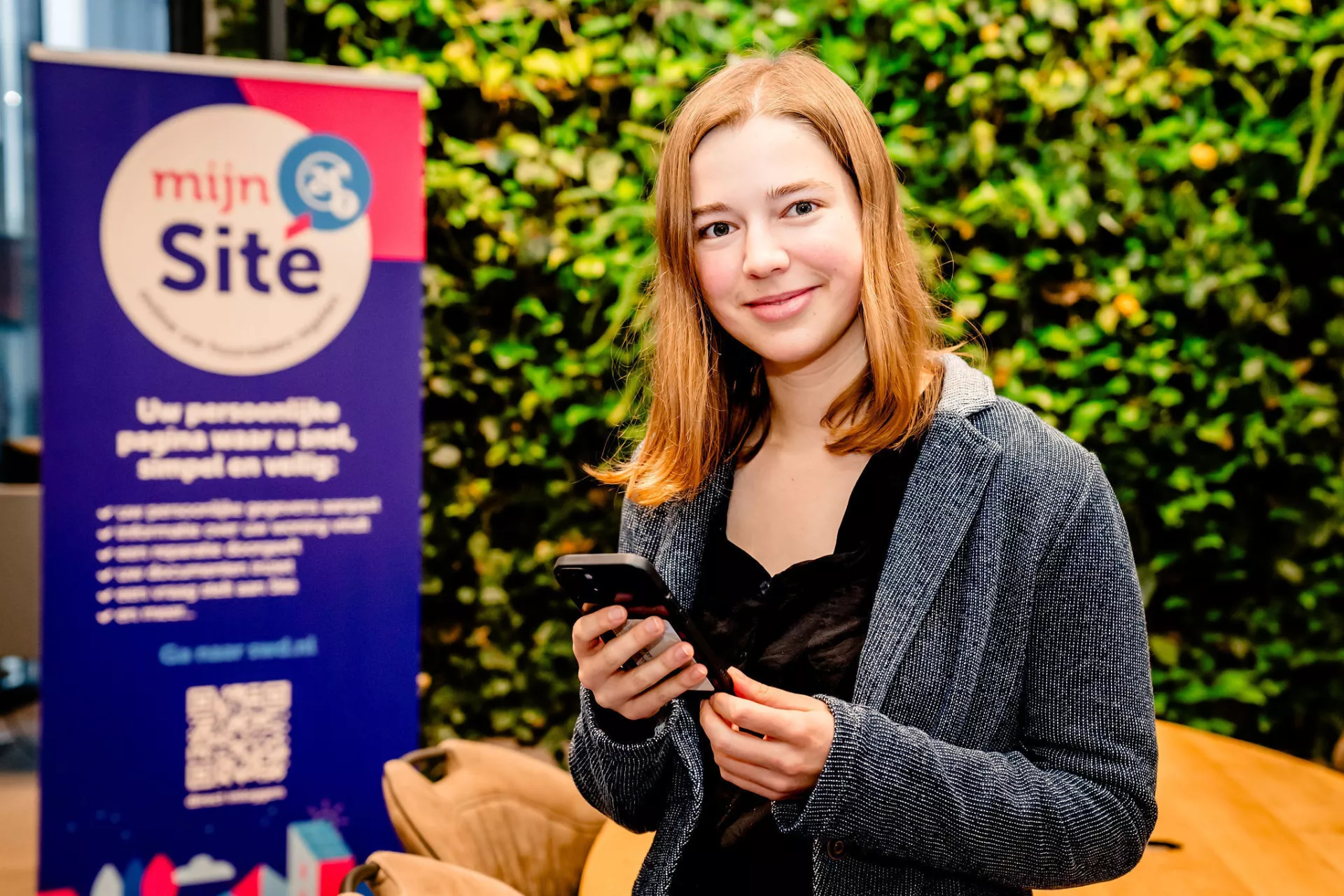 Dame met een mobiele telefoon in haar hand staat voor een groene kantoorwand