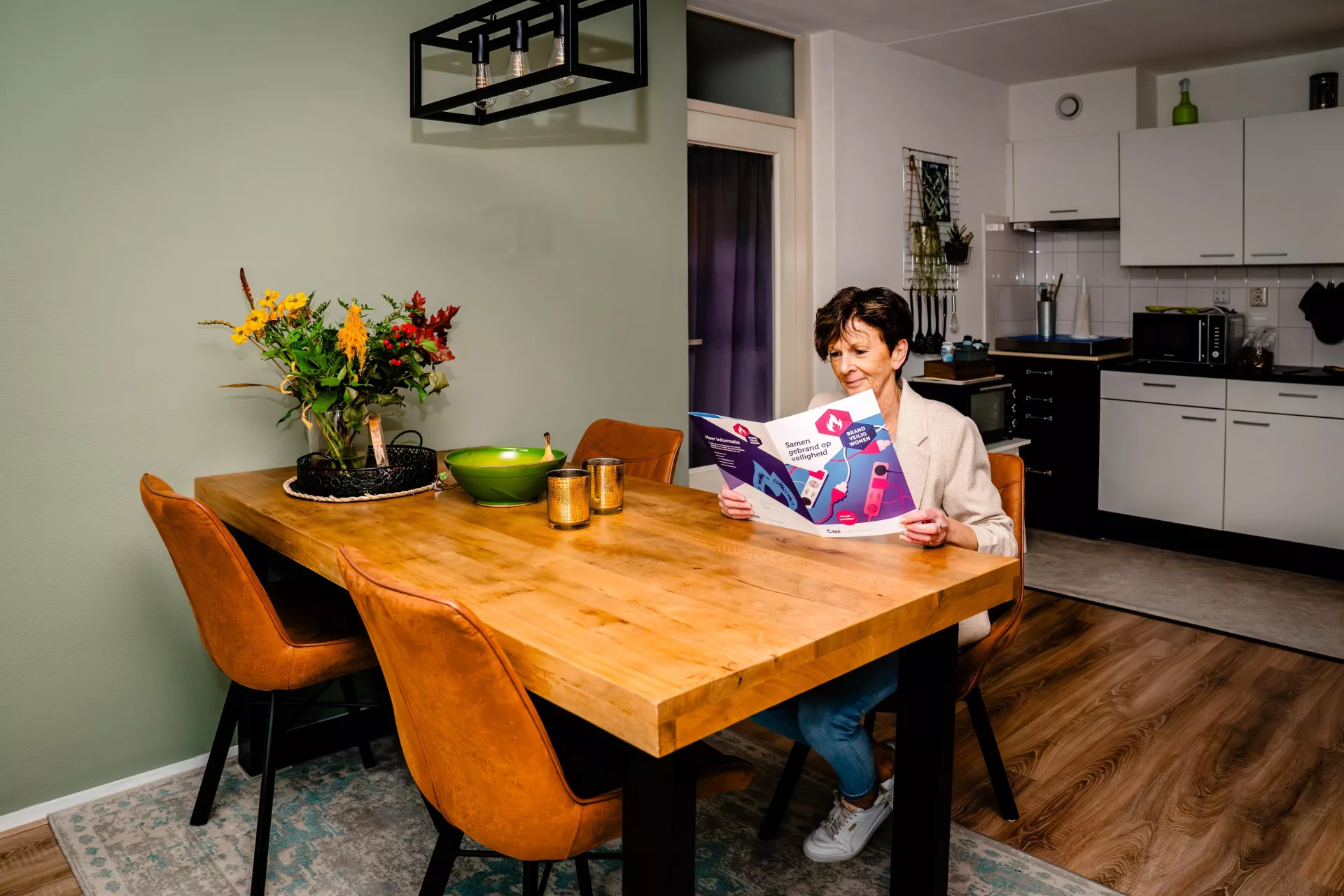 Een mevrouw leest een folder aan een houten tafel in haar keuken