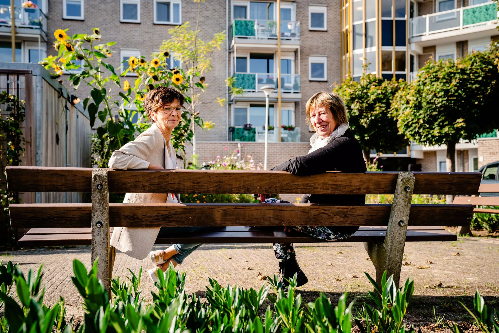 Twee dames zitten op een bank voor een appartementengebouw